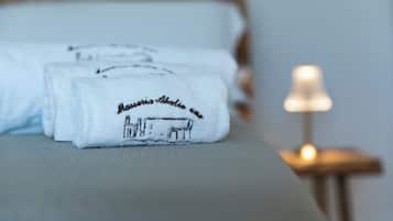 Neatly folded towels with embroidered text on a bed, a bedside lamp, and a wooden nightstand.