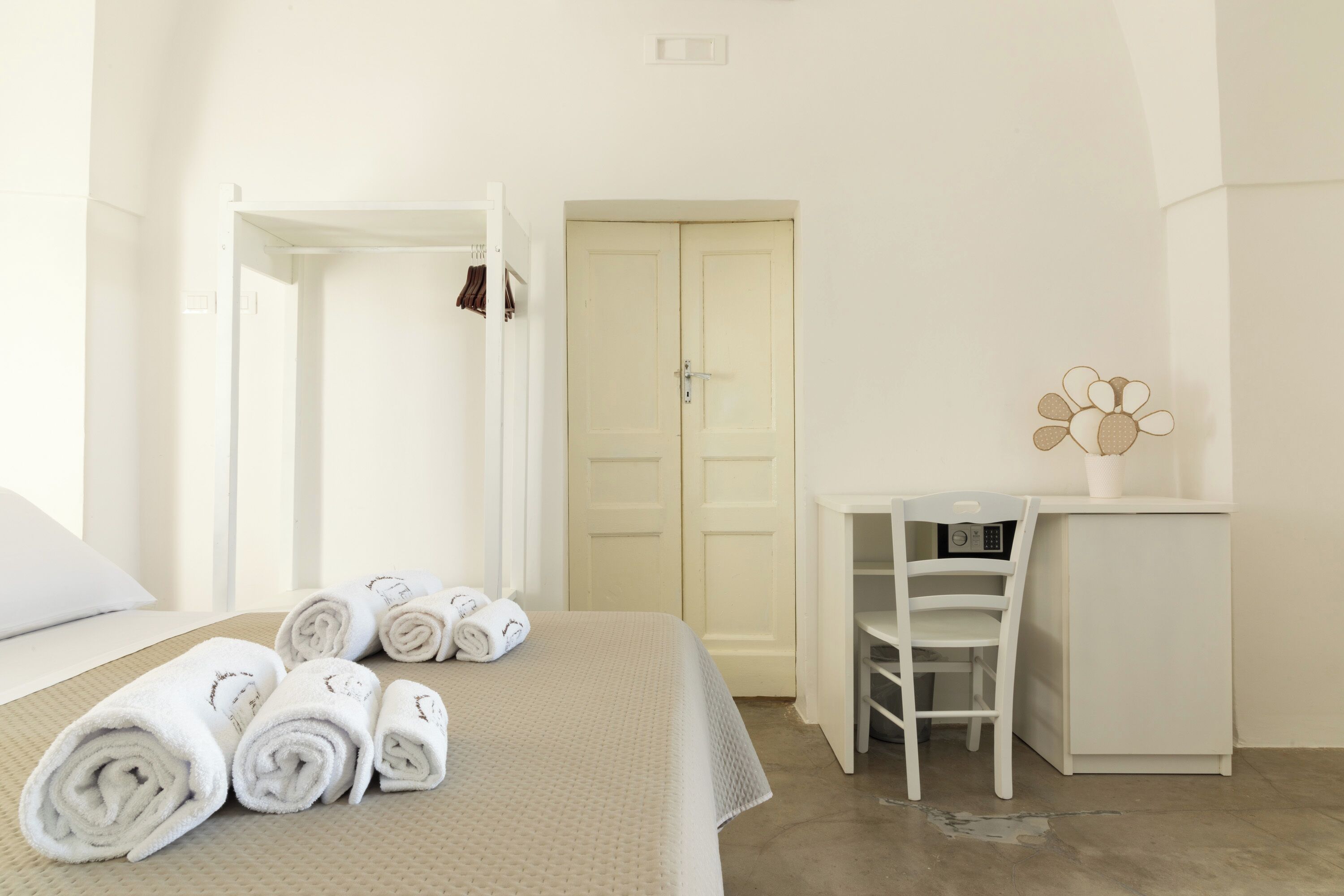 A hotel room with a bed, rolled towels, a desk, and a chair.