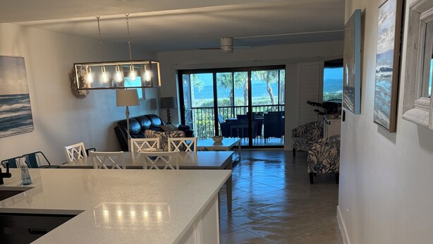 A modern kitchen with a large island, dining area with chairs, and a view of the ocean through large sliding doors.