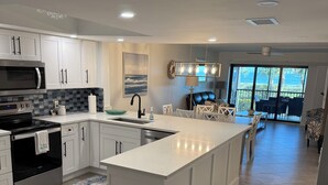 A modern kitchen with white cabinetry, a large island, and a dining area with a view to the outdoors.