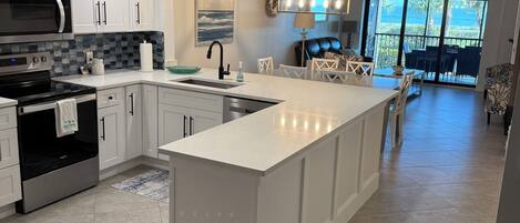 A modern kitchen with white cabinetry, a large island, and a dining area with a view to the outdoors.