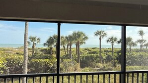 A view from a balcony with a railing, overlooking a beach with palm trees and a clear sky.
