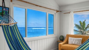 A room with a hammock, a striped chair, and a view of the ocean through large windows. - Summer Deal Oceanfront Kauai 2BR Home with Direct Beach Access (Anahola)