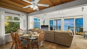 A spacious living area with a large window overlooking the ocean, a dining table with chairs, and a cozy seating area. - Summer Deal Oceanfront Kauai 2BR Home with Direct Beach Access (Anahola)