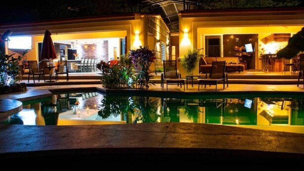 Ein Poolbereich mit Terrasse, Sitzgelegenheiten im Freien und einem gut beleuchteten Innenraum.