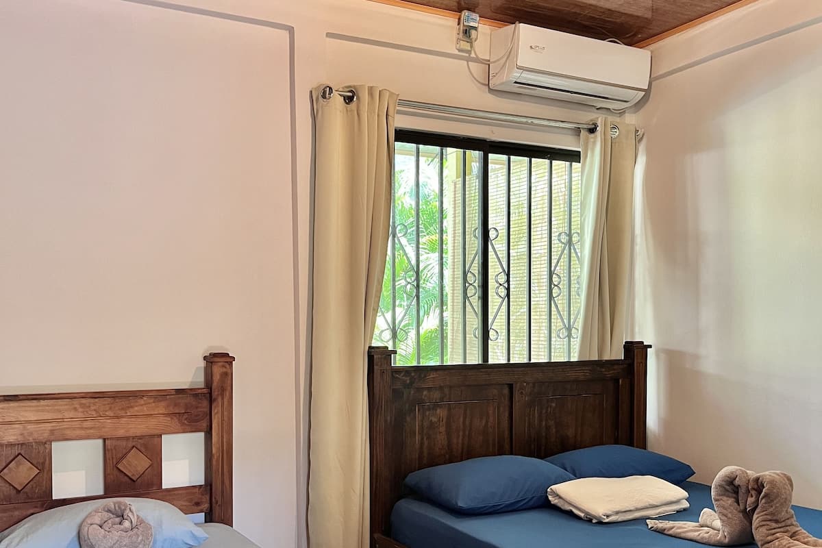 A bedroom with two beds, a window with metal bars, an air conditioning unit, and a ceiling light.