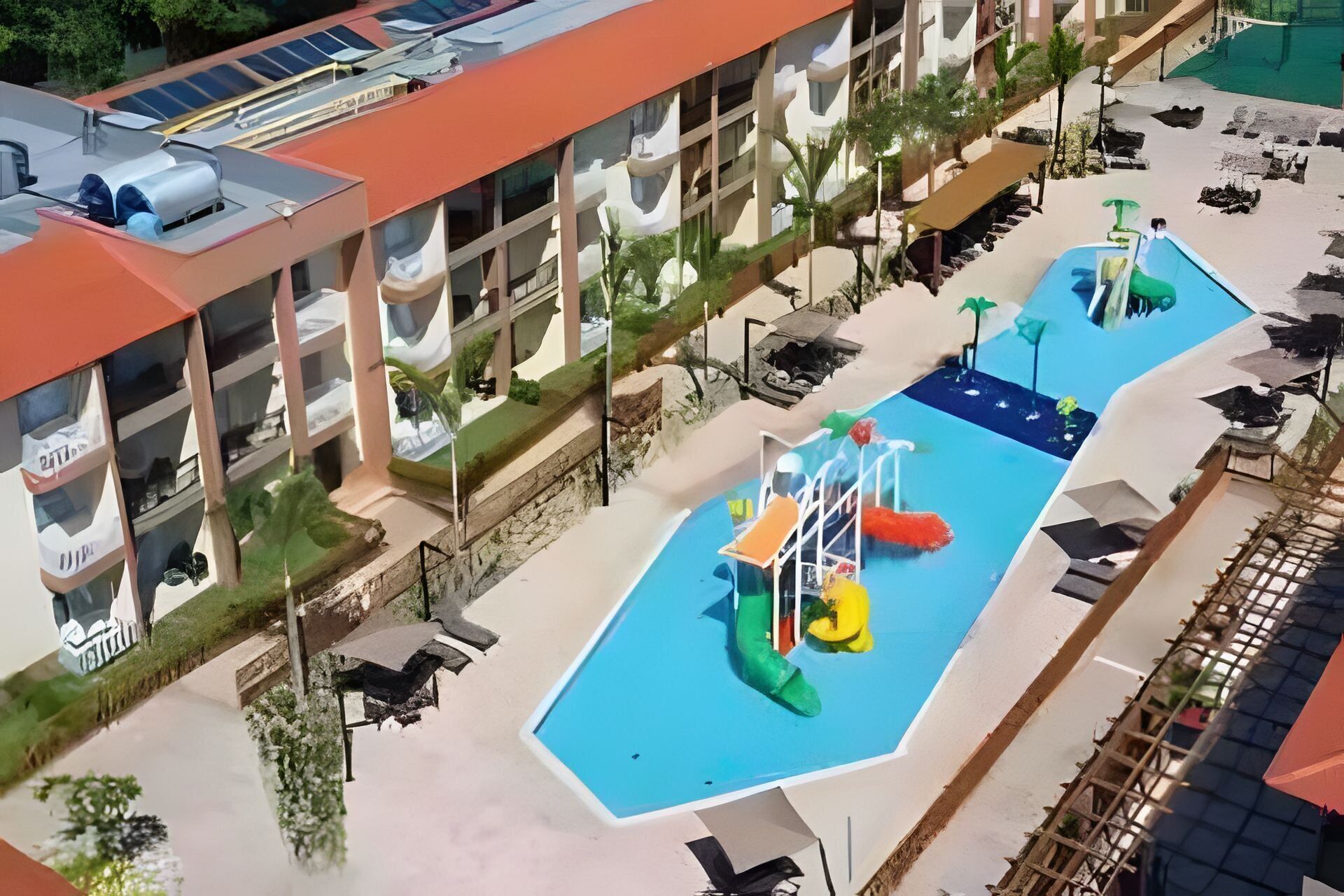 Uma área de piscina no terraço com escorrega e estruturas de recreação, cercada por um edifício com várias varandas.