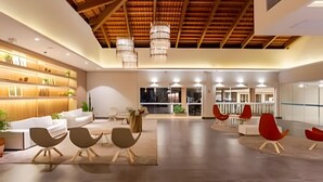 A spacious lobby with a high ceiling, modern furniture, and a view of the cityscape through large windows. - Ondas Praia Resort (Porto Seguro)