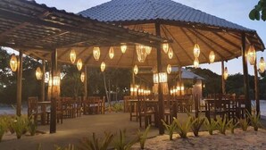An outdoor dining area with wooden tables and chairs, covered by a pergola with hanging lanterns. - Ondas Praia Resort (Porto Seguro)
