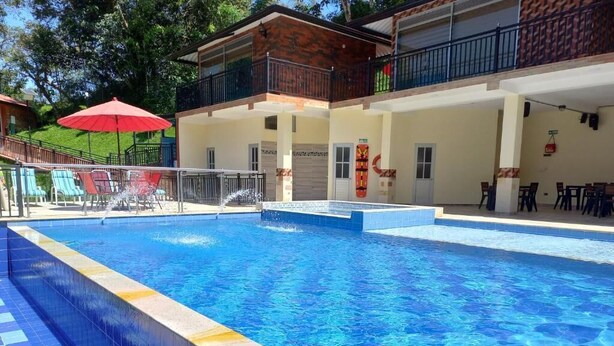 A swimming pool with a tiled edge, a red umbrella, and a building with a balcony in the background.