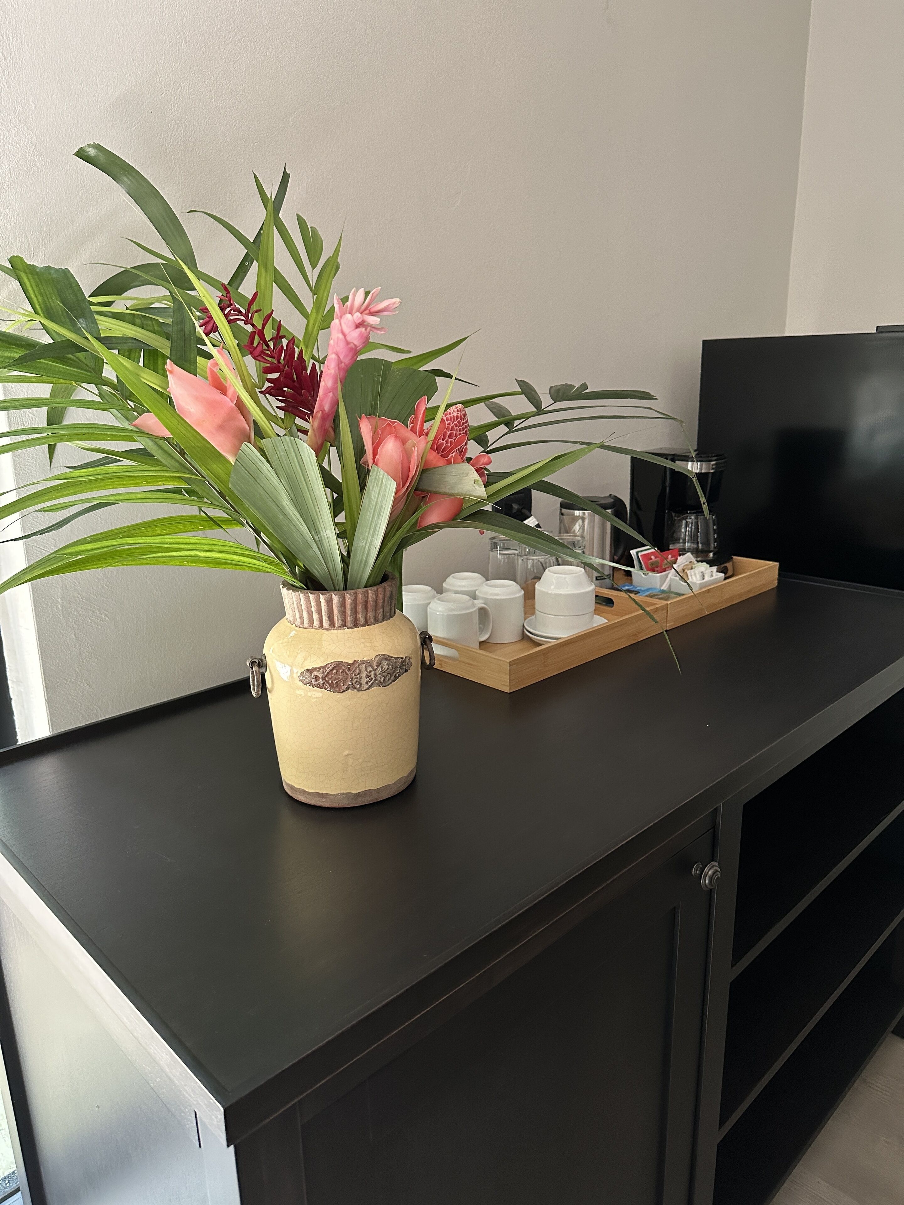 A kitchen counter with a decorative vase of flowers, a coffee maker, and a tray with cups and saucers.