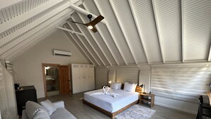 A spacious bedroom with a large bed, a sofa, a wooden desk, and a ceiling fan. - HADCO Experiences at AWNC (Lopinot)