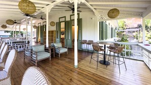 A covered outdoor seating area with wicker furniture, wooden flooring, and green shutters. - HADCO Experiences at AWNC (Lopinot)