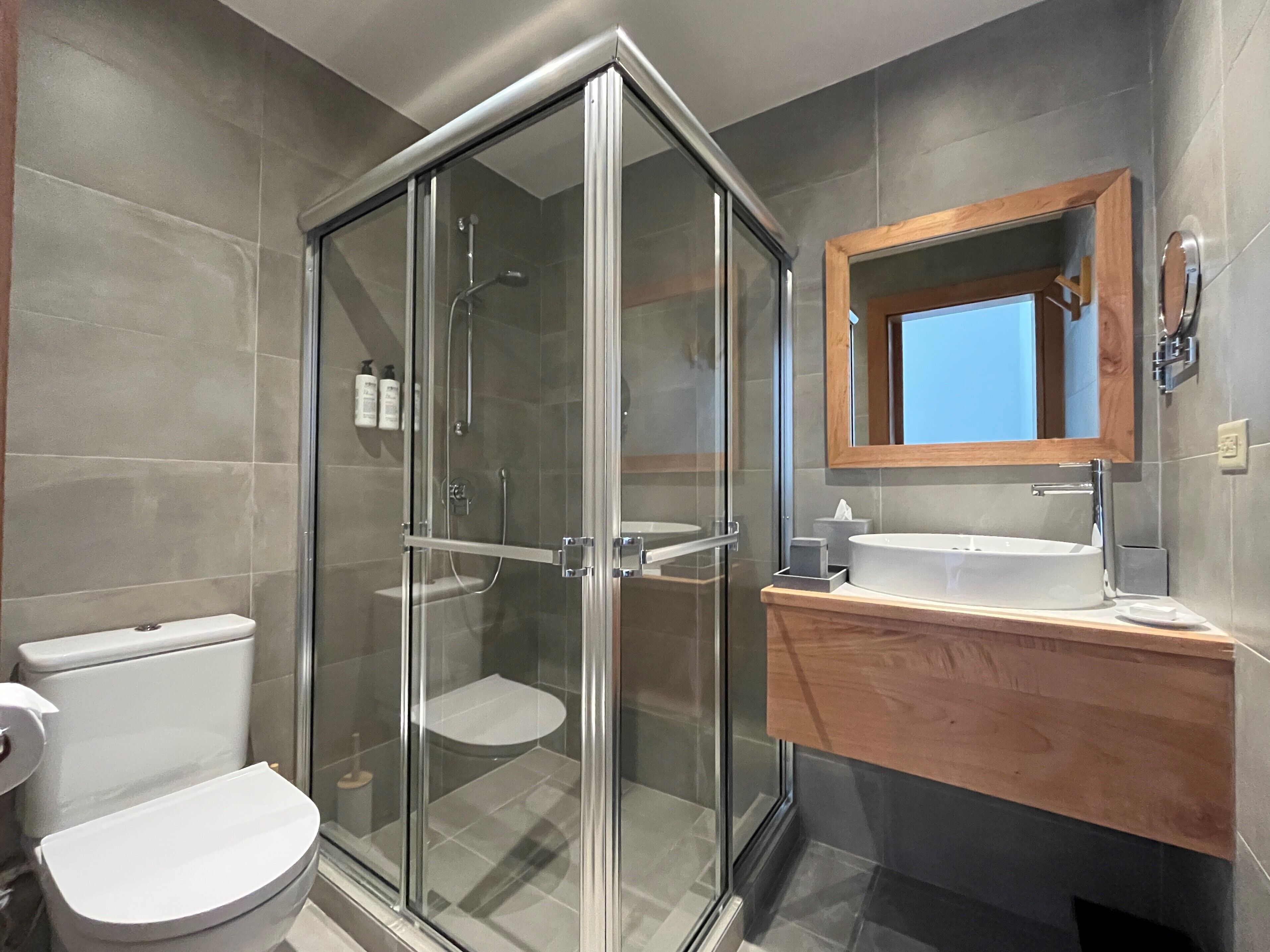 A modern bathroom with a glass-enclosed shower, a white toilet, and a wooden vanity with a mirror.