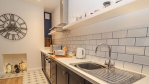 A modern kitchen with a large wall clock, a built-in sink, and a tiled backsplash. - The Hare (Nantwich)