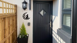 A black door with a diamond-shaped window, a wooden fence, a wall-mounted lantern, and a potted plant with flowers. - The Hare (Nantwich)