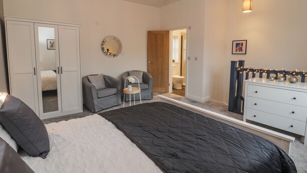 A bedroom with a large bed, two armchairs, a dresser, a chandelier, and a mirror on the wall. - The Hare (Nantwich)