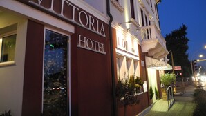 Exterior del Hotel Vittoria, con un letrero llamativo, una escalera que conduce a la entrada y una vista de la calle con semáforos.