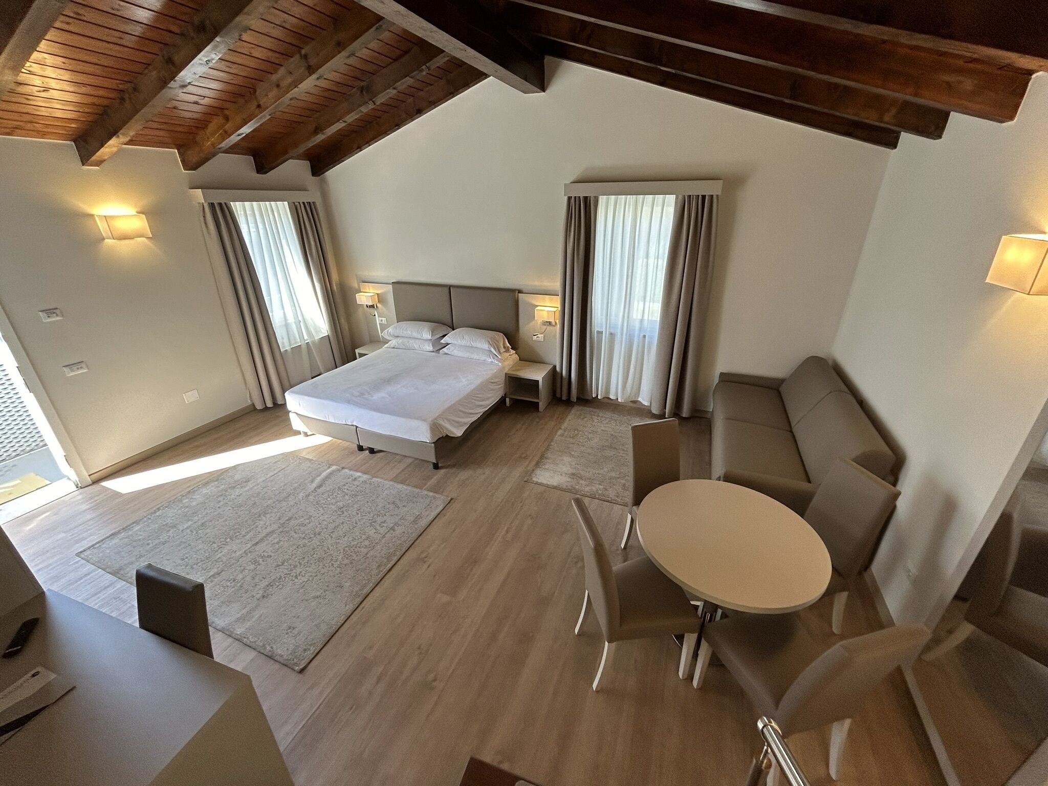 A modern bedroom with a bed, bedside tables, a sofa, a small table, and a view of the outside.