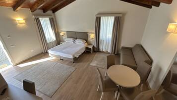 A modern bedroom with a bed, bedside tables, a sofa, a small table, and a view of the outside.