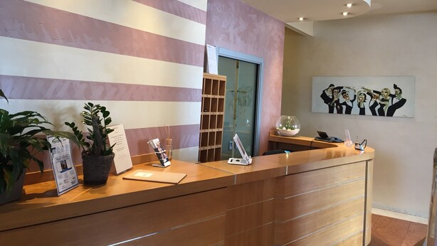 A hotel reception desk with a striped wall, a glass door, and a framed artwork above it. - La  casetta  (Rubano)