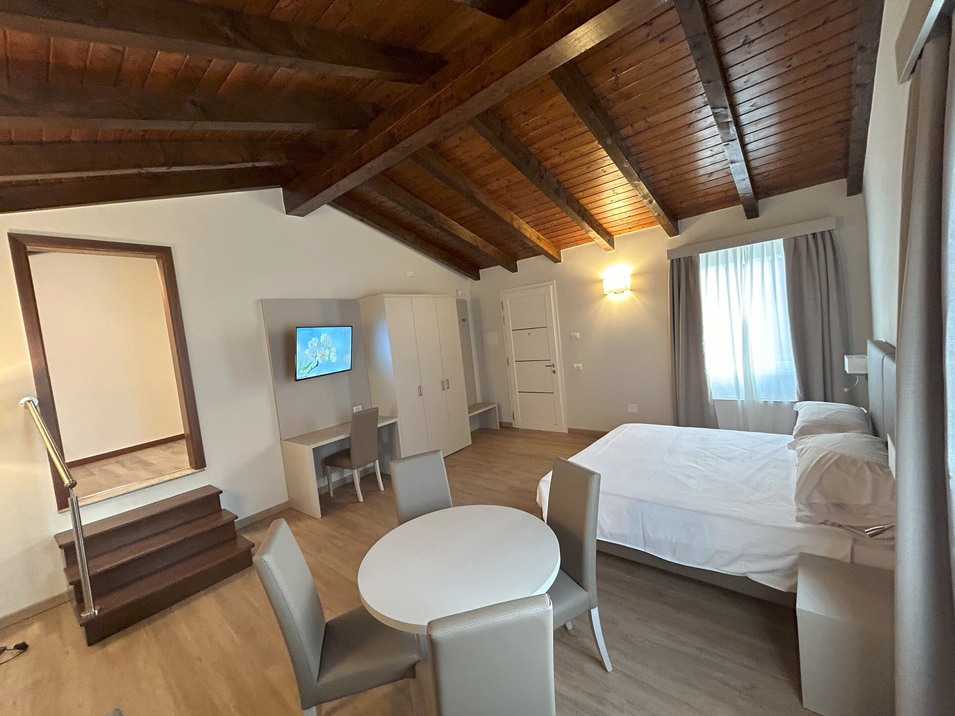 A hotel room with a bed, a desk with a chair, a TV, and a wardrobe.