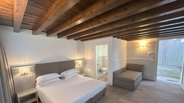 Un dormitorio con cama, mesitas de noche, un área de descanso con una silla y vistas al exterior.