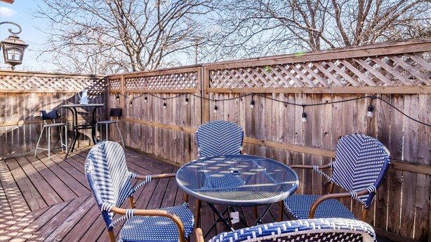 A wooden deck with a round table and four chairs, a small table with chairs, and a wooden fence with a lattice top.