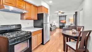 A modern kitchen with wooden cabinets, a stainless steel refrigerator, a gas stove, and a dining area with a table and chairs.