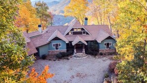A two-story house with a stone foundation and a steeply pitched roof, surrounded by autumn foliage and mountains in the background. - Amazing views at L’Oursière in Bear Lake Reserve, from the new  hot tub. (Tuckasegee)