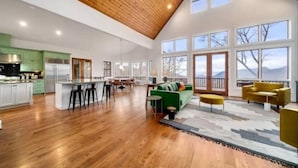 A spacious living area with a wooden ceiling, large windows, a green sofa, and a yellow armchair. - Amazing views at L’Oursière in Bear Lake Reserve, from the new  hot tub. (Tuckasegee)