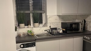 A compact kitchen with a washing machine, a microwave, and a sink. - Deptford - 1 Bed - 1 Bathroom - Parking (London)