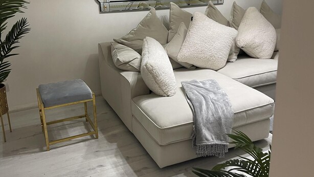 A modern living room with a white sofa, a small wooden stool, and a large mirror with a decorative frame. - Deptford - 1 Bed - 1 Bathroom - Parking (London)