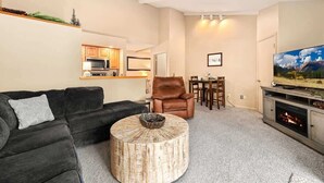 Ein Wohnzimmer mit dunklem Sofa, rundem Couchtisch, braunem Ledersessel, einem Esstisch mit Stühlen, einem Kamin und einem Fernseher.