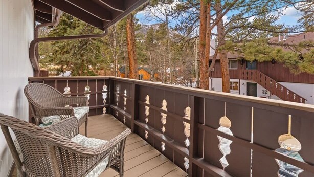 Ein Balkon mit Korbstühlen und einem Tisch, mit Blick auf eine bewaldete Gegend mit hohen Bäumen und einem Gebäude im Hintergrund.
