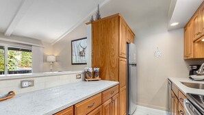 Eine Küche mit Holzausstattung, einem Kühlschrank, einer Spüle und einem Fenster mit Blick auf Bäume.