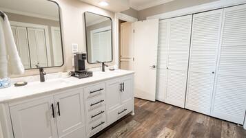 Une salle de bain avec un meuble-lavabo blanc, un grand miroir, un évier et des toilettes. Il y a deux portes blanches et un plancher en bois.