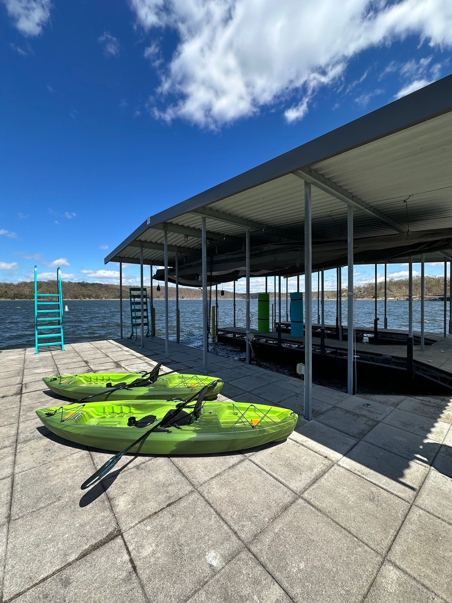Un muelle techado con kayaks y una escalera, con vista a una masa de agua.