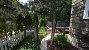 A garden pathway leading to a wooden deck with a white picket fence on one side.