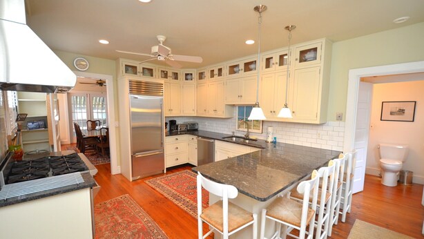A kitchen with a central island, white cabinets, a stainless steel refrigerator, and a ceiling fan.