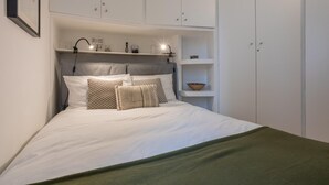 A neatly made bed with white bedding and a green throw blanket. There are multiple shelves above the bed with various items. - Dora Apartment by Wonderful Italy (Turin)
