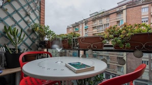 A balcony with a round table, red chairs, and potted plants. - Dora Apartment by Wonderful Italy (Turin)