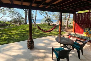 A covered patio with a hammock, outdoor seating, and a view of the ocean. - Beachfront Apartment 1 Bedroom - Mariposa (Playa Tamarindo)
