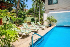 A pool area with lounge chairs and palm trees. - Beachfront Apartment 1 Bedroom - Mariposa (Playa Tamarindo)