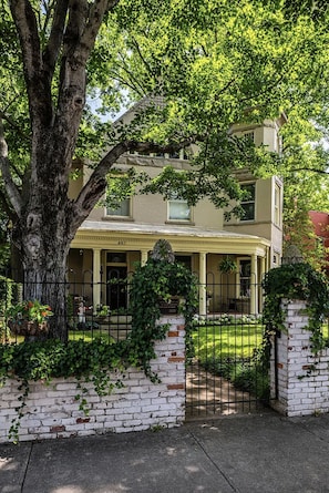 A two-story house with a covered porch, a brick wall with greenery, and a metal gate. - Historic Ward Home - Experience history in the horse country! 5br 5.5bth (Lexington)