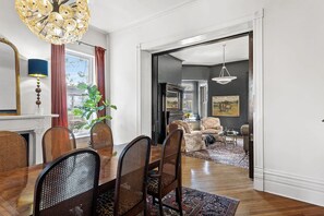 A dining area with a wooden table and chairs, a chandelier, and a view of the living room through an open doorway.