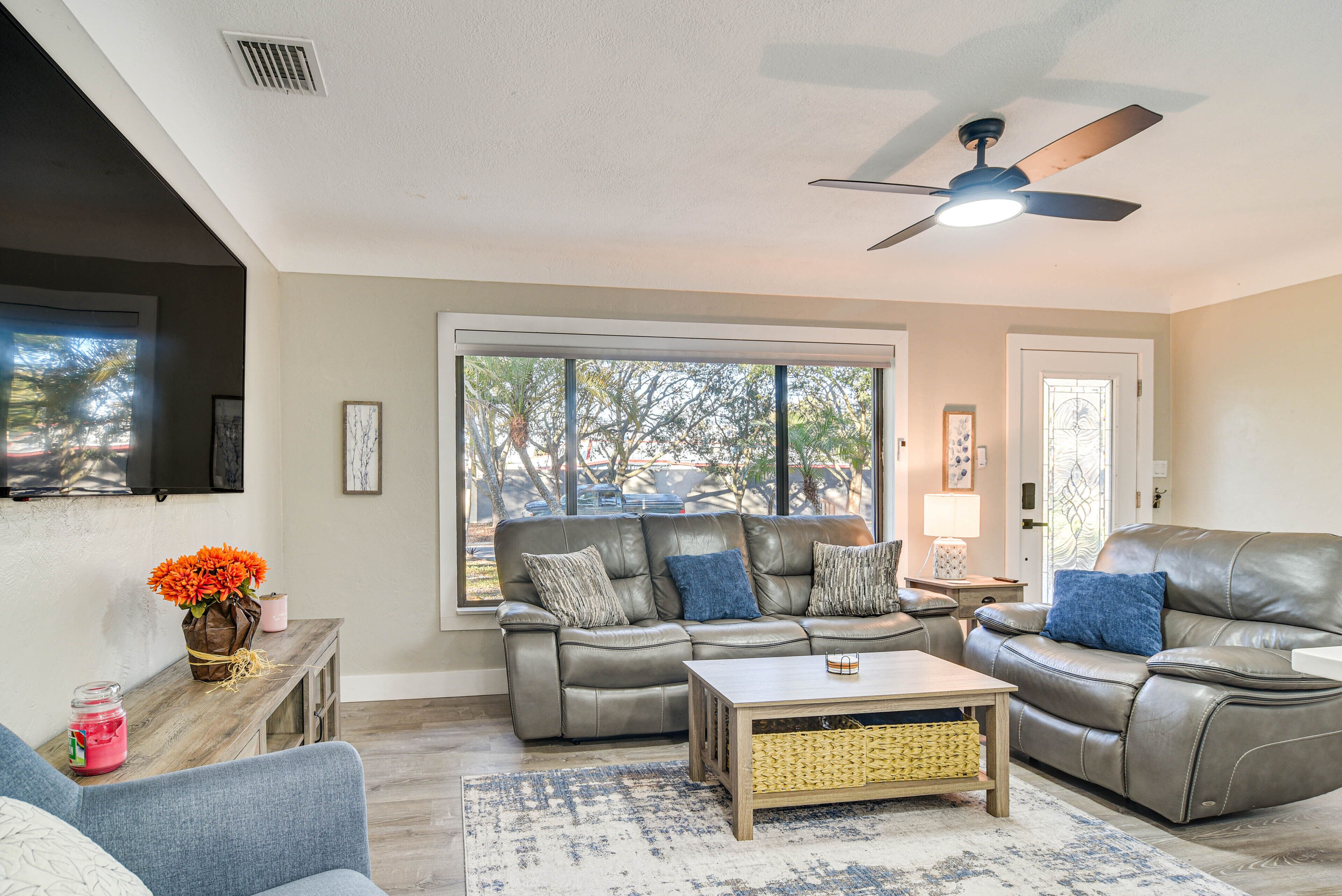 A living room with a grey leather sofa, a blue armchair, a wooden coffee table, and a large window with a view of trees.