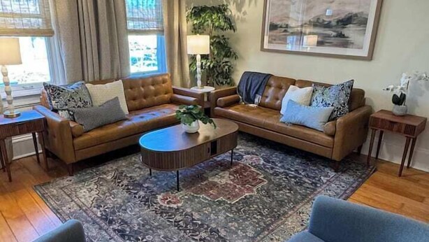 A living room with a brown leather sofa, a blue armchair, a coffee table, and a ceiling fan. - Elegant Brady St Home with Excellent Walkability (Milwaukee)