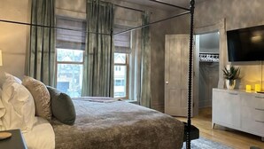 A bedroom with a four-poster bed, a ceiling fan, a TV, and a view of the outside through large windows. - Gorgeous Brewers Hill Victorian (Milwaukee)