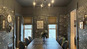 A dining room with a long wooden table, six chairs, a chandelier, and patterned wallpaper. - Gorgeous Brewers Hill Victorian (Milwaukee)